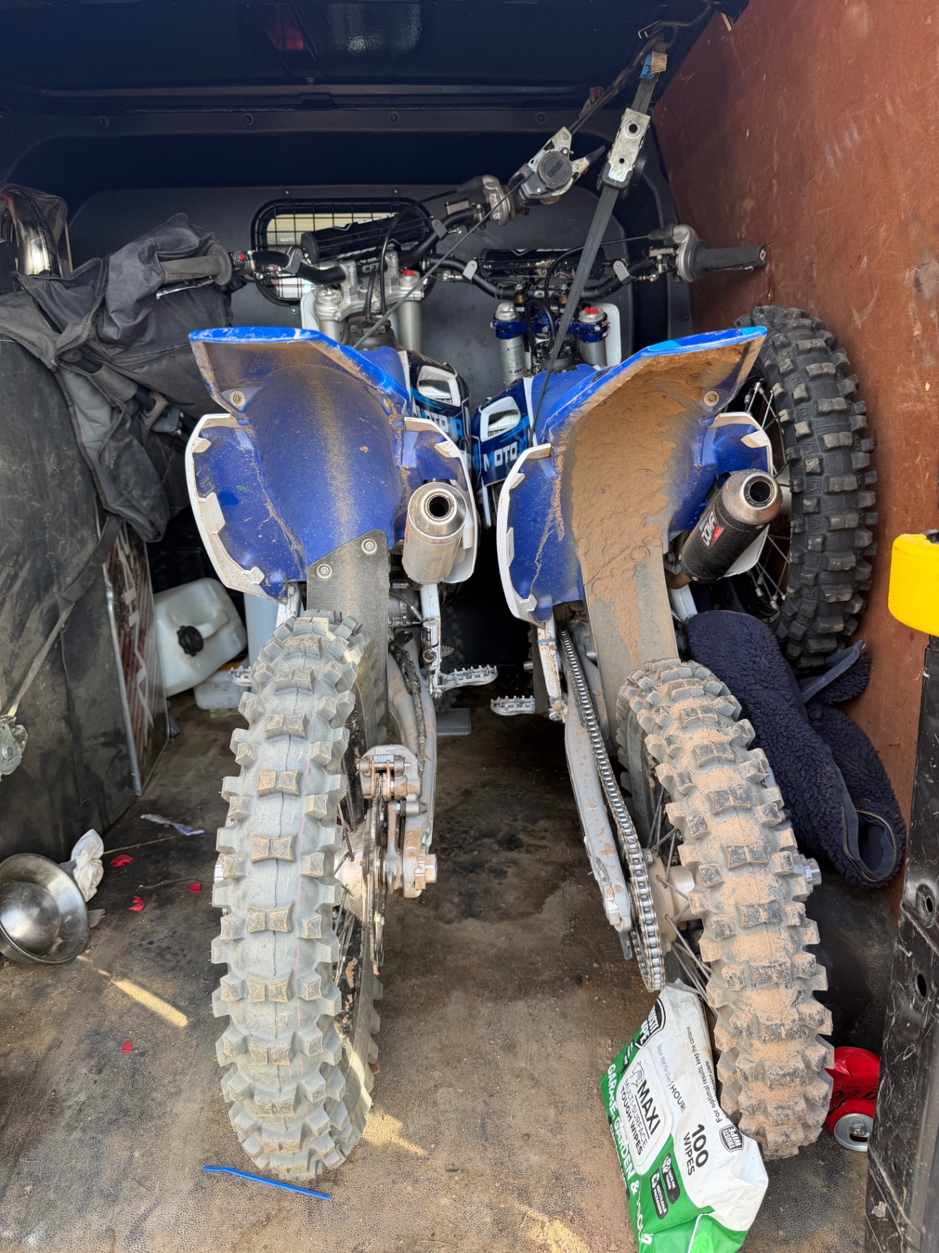 Rear view of two muddy blue motocross bikes secured inside a van.